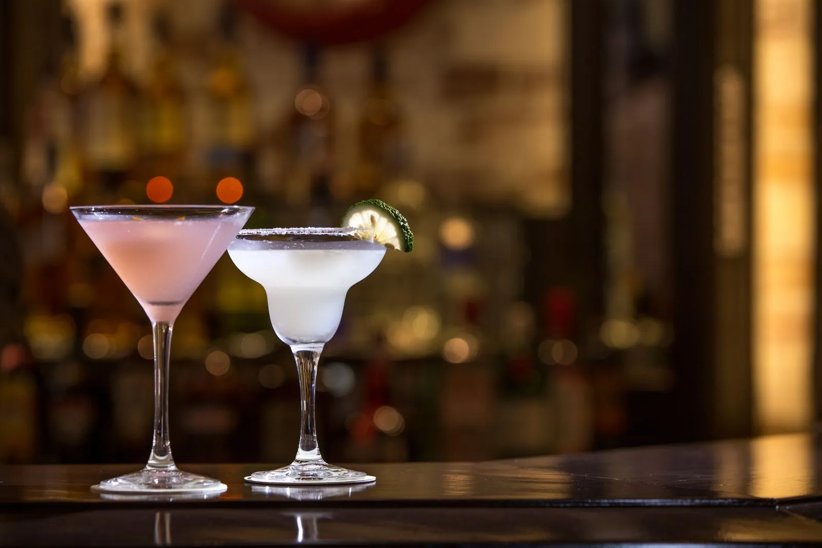 Two cocktails with lime garnish on a bar, set against a blurred background. Perfect for nightlife scenes.
